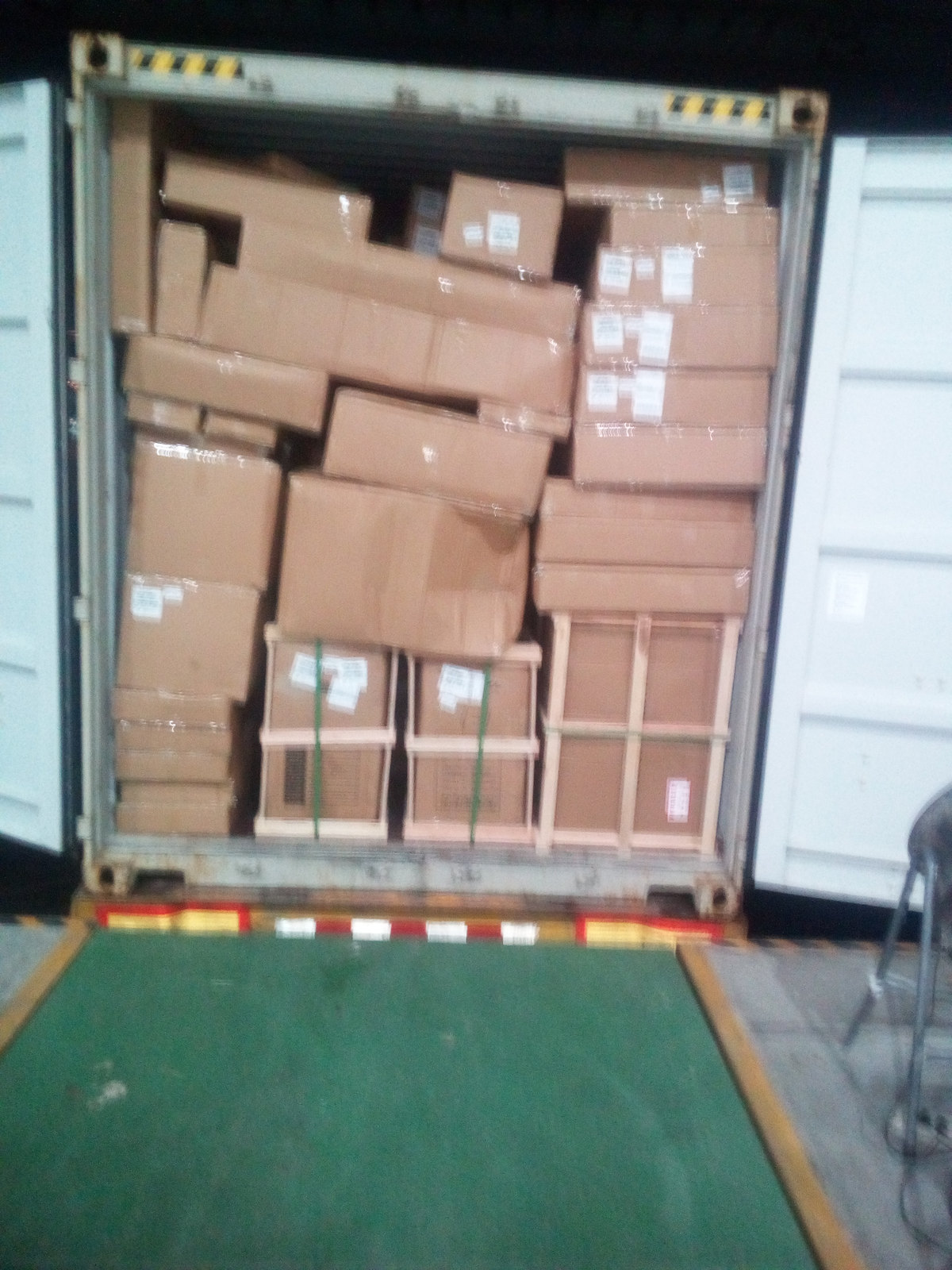 Cartons stacked inside a container with a timber pallet base visible at the door